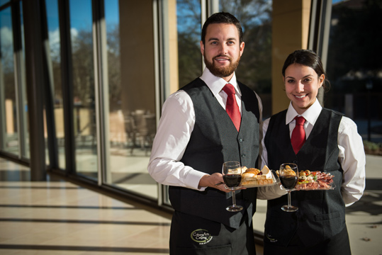 Two servers holding appetizers and wine.